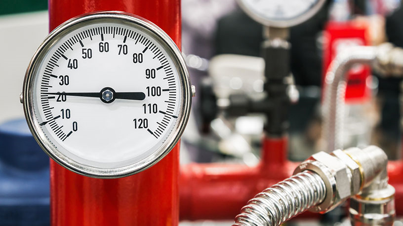 Nahaufnahme eines Manometers an einem roten Rohr in einer industriellen Umgebung.