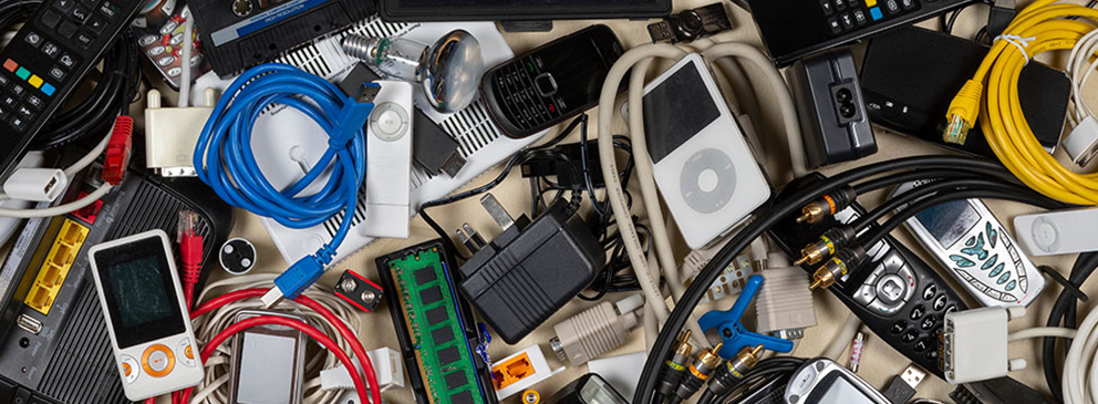 Ansammlung verschiedenster elektronischer Geräte und Kabel, darunter Mobiltelefone, Fernbedienungen und Netzwerkkabel.