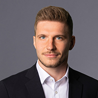 Marc Kaczorowski in einem dunklen Anzug mit weißem Hemd, vor einem grauen Hintergrund.