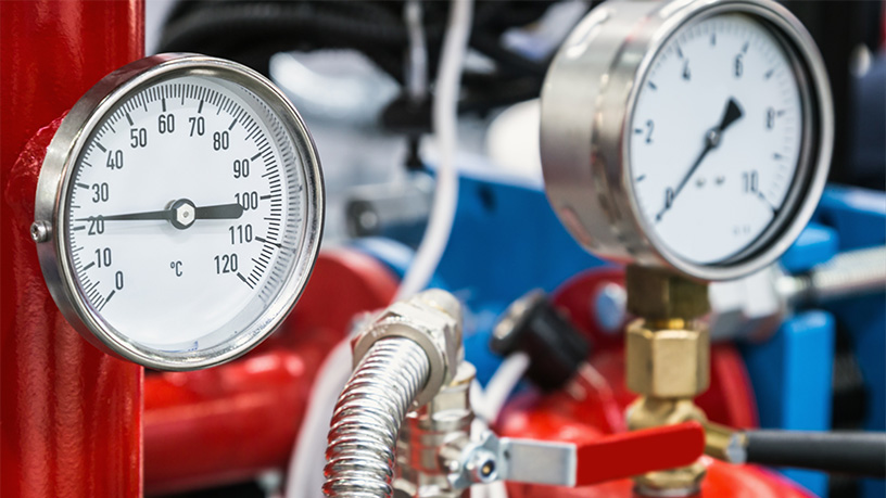 Industrie-Manometer und Thermometer auf rotem und blauem Hintergrund für präzise Temperatur- und Druckmessung.