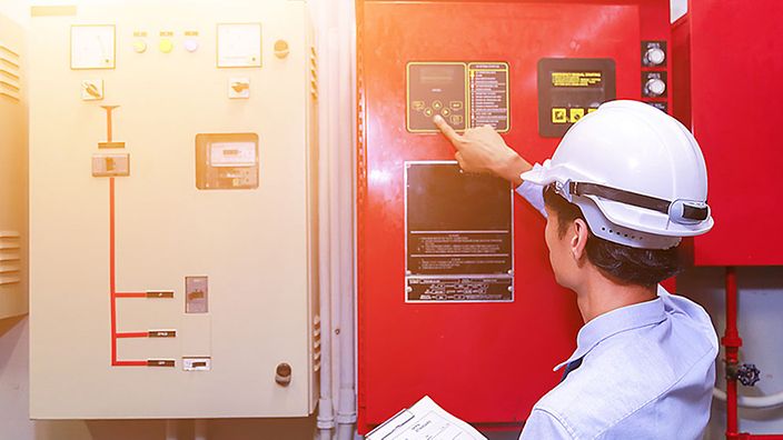 Ingenieur mit Schutzhelm überprüft ein Steuerpanel.