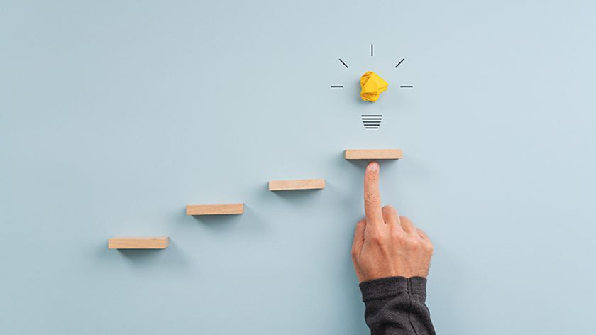 Freischwebende Stufen an einer Wand. Finger zeigt von unten auf die oberste Stufe und auf der das Symbol einer Glühbirne ist. 